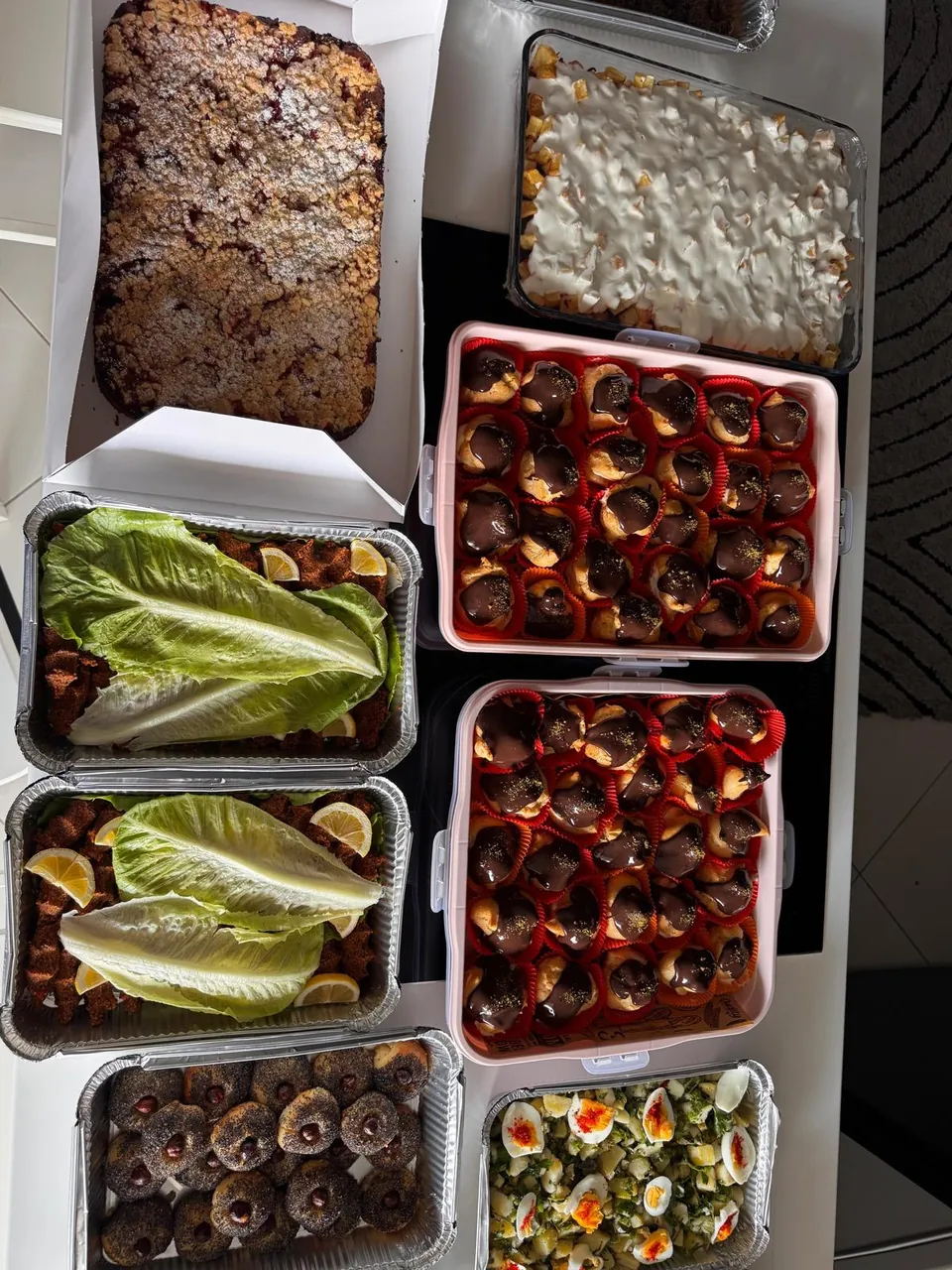 Üstten görünüm: çikolata soslu profiteroller, kırıntılı tart, köfte, kurabiye ve patates salatası tepsileri