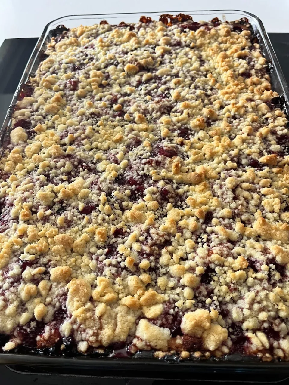 Cam fırın kabında altın renkli kırıntılarla kaplı vişneli tart