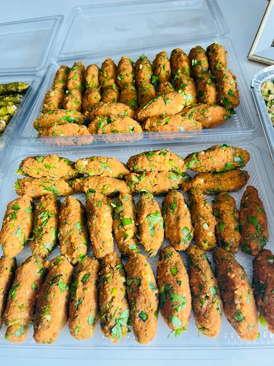 Kaplarda sıra sıra dizilmiş, maydanoz ve yeşil soğanlı turuncu mercimek köfteleri