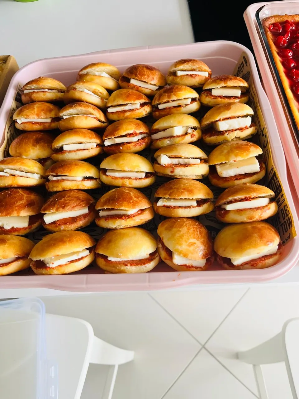 Pembe tepside sıra sıra dizilmiş, içinde ezme ve peynir dilimi bulunan mini sandviç poğaçalar