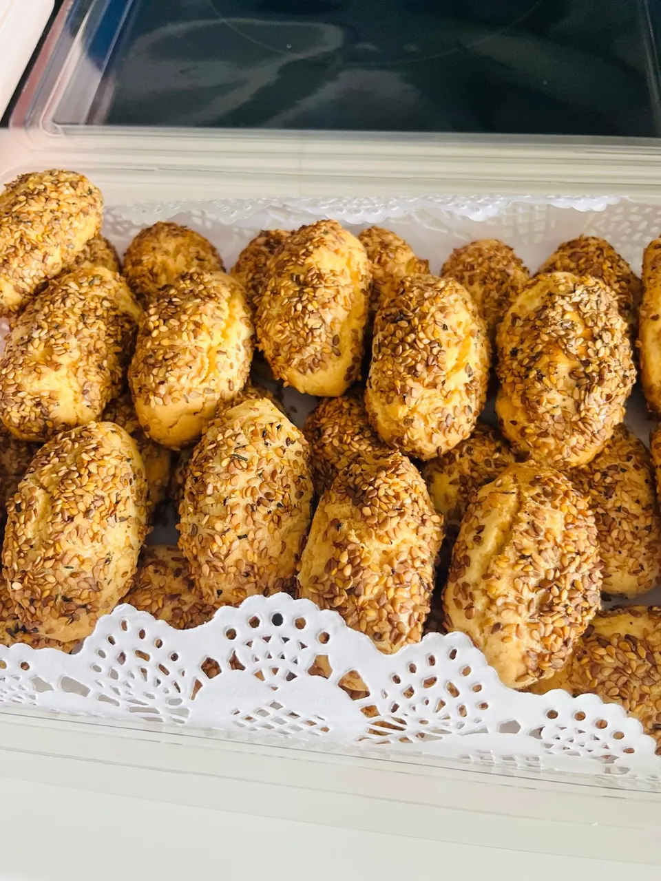Dantel kağıtlı kapta, üzeri bol susamlı altın renkli minik poğaçalar